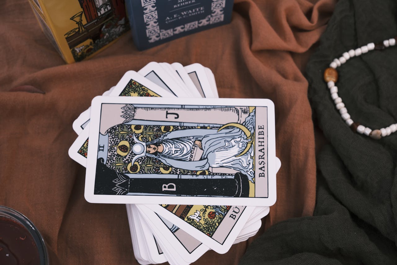 Deck of tarot cards spread on brown fabric with beads, emphasizing divination.